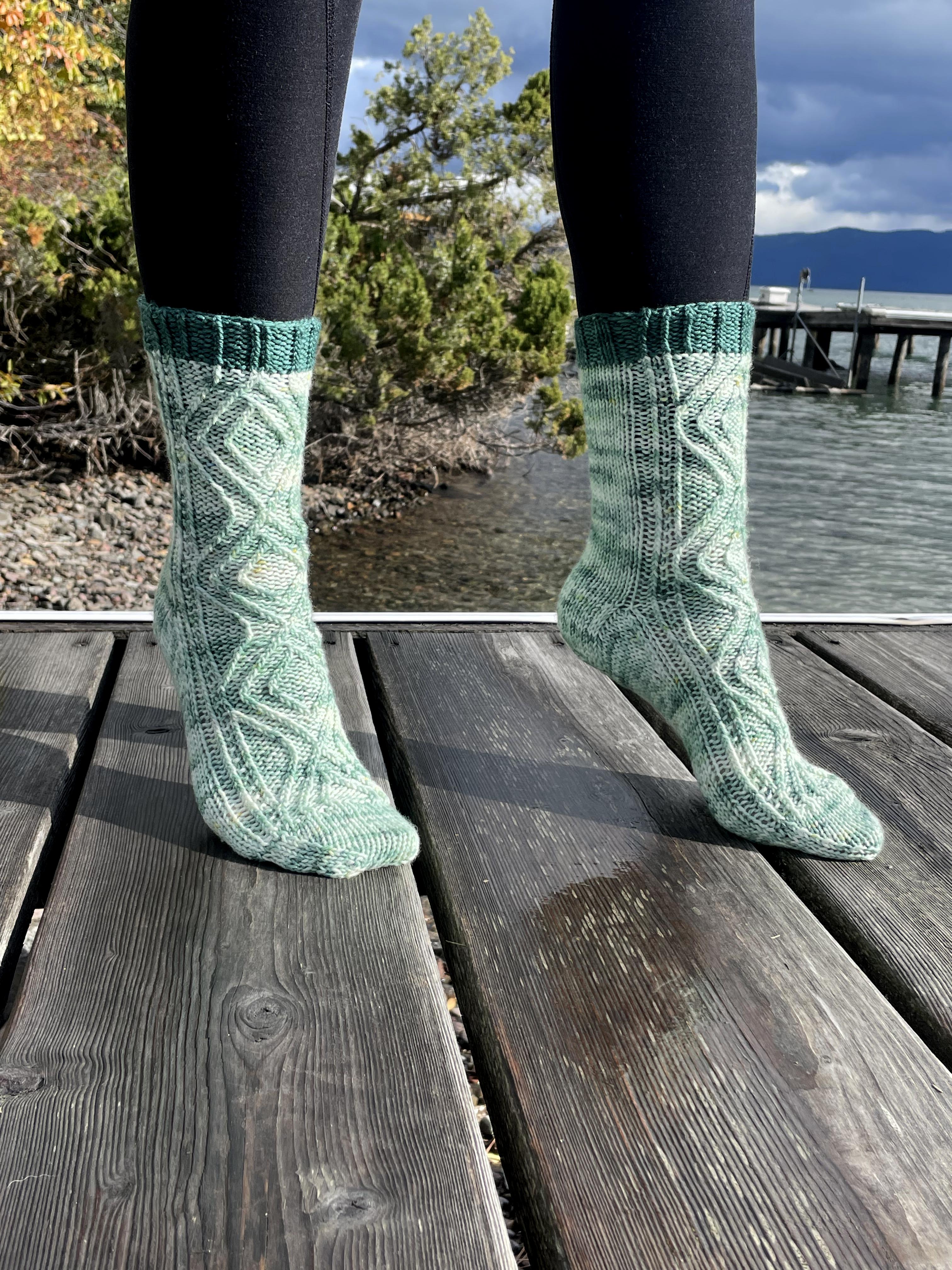 Green knitted socks worn on a wooden dock with a scenic background
