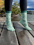 Green knitted socks worn on a wooden dock with a scenic background